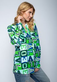 Koszula z długim rękawem z kolorowym geometrycznym wzorem w odcieniach zieleni i niebieskiego, wykonana z gładkiego materiału, o luźnym kroju i kołnierzyku.