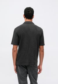 Sort skjorte med kort erm i svart, med teksturert mønster. Har en klassisk krage, ubelagt kant, og er kombinert med mørke denimjeans.