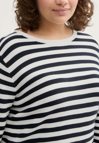 Schwarz-weißer gestreifter Pullover mit rundem Ausschnitt, texturiertem Stoff und subtilen Rippungen. Die Streifen haben die gleiche Breite und erzeugen ein einheitliches Muster.