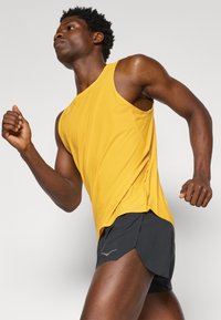Yellow sleeveless athletic top with a smooth texture, paired with black running shorts featuring a side split and grey logo detail.
