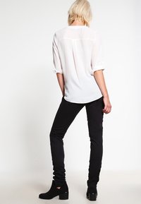 Vit, lätt blus med uppvikta ärmar och en ryggås detail, i kombination med svarta, figursydda byxor och ankelboots med klack.