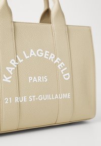 Sac fourre-tout en cuir texturé beige avec deux poignées solides. Présente un logo en relief blanc : "KARL LAGERFELD PARIS 21 RUE ST-GUILLAUME."