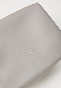Grijze waterdichte tas met een minimalistisch ontwerp, featuring een gladde textuur en het geprofileerde "RAINS" logo. Eenvoudige, rechthoekige vorm zonder hardware.