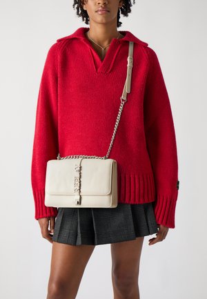 Pull en tricot rouge avec un col en V et un ourlet côtelé, associé à une jupe écossaise noire. Un sac bandoulière beige avec une chaîne comme anse et des détails de logo.