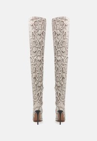 Botas hasta la rodilla con textura, hechas de tela con estampado de serpiente en beige y gris. Cuentan con un tacón de aguja y un detalle de cremallera expuesta en la parte trasera.