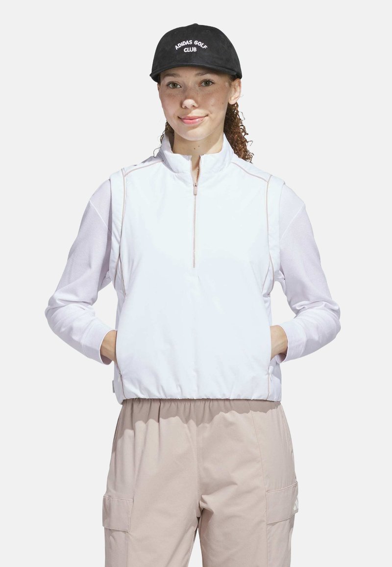 Hvid zip-up jakke med en struktureret krop, lange mesh ærmer og kontrasterende sømme. Båret med lyse beige bukser og en sort cap med hvid tekst.