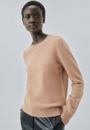 Light pink cashmere sweater with long sleeves, round neckline, and ribbed hem. Worn over black trousers, featuring a smooth texture.