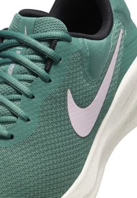 Grön sportskor med mesh-övre del, platta snören och en rosa Nike-logotyp. Har en gummisula med lätt textur och skumdämpning.