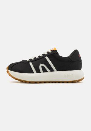 Black sneaker with white accents, a thick white sole, textured gum rubber outsole, and orange tag on the tongue. Features classic lace closure.