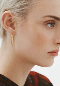 Pendientes alargados en tono dorado con un diseño minimalista, que presentan una superficie lisa y brillante y una forma elegante, similar a un clip de papel.