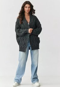 Sweter w warkocze w ciemnoszarym kolorze, o luźnym kroju, szerokich rękawach i teksturowanym wzorze. W połączeniu z jasnoniebieskimi spodniami o szerokich nogawkach.