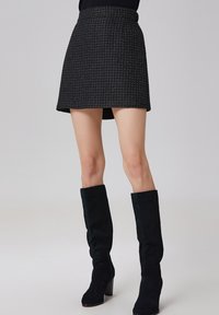 Une mini-jupe en tweed noir avec une taille structurée et un design évasé. À associer avec des bottes en daim noir jusqu'aux genoux avec des talons épais.