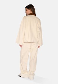 Crème-kleurige, oversized jas en bijpassende broek, vervaardigd uit zachte stof met een relaxte pasvorm. Opvallend bruin kraagdetail.