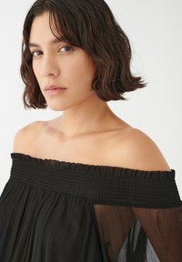 Juodas off-the-shoulder palaidinė su smulkios klostės liemeniu, permatoma medžiaga ir raukšlėta apykakle, turinti laisvai krentančias rankoves ir lengvą tekstūrą.