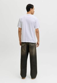 Camiseta de algodón blanca de manga corta, combinada con unos vaqueros de mezclilla de ajuste holgado con un degradado de oscuro a claro, que cuentan con dos bolsillos traseros.