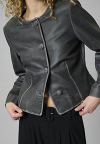 Gray leather jacket with round neckline, two front buttons, and visible stitching details. Paired with black trousers featuring a belt.