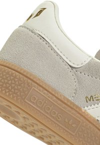 Talons de baskets Adidas en suède gris clair et cuir blanc avec semelle en gomme et détails de marque métalliques dorés.