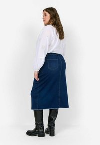 Tumed sinine denim seelik, millel on sobiv lõige ja taga lõhik. Kombineeritud valge pluusiga, millel on ringikujulised lõikeavad. Mustad põlve kõrgustele ulatuvad saapad.