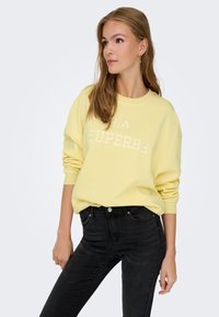 Sweatshirt galben cu guler rotund, inscripționat cu textul "LA SUPERBEE", asortat cu blugi negri slim-fit. Material din bumbac, croială relaxată, manșete ribbate.