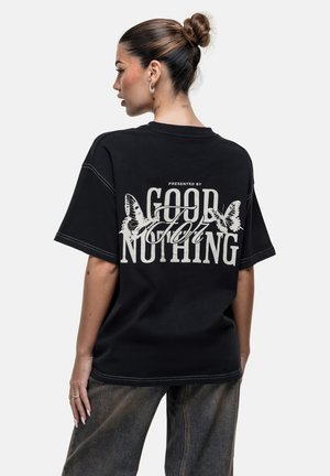 Zwarte oversized t-shirt met korte mouwen, voorzien van witte grafische tekst en vlinderontwerpen op de achterkant. Verweerde stiksels als accent.