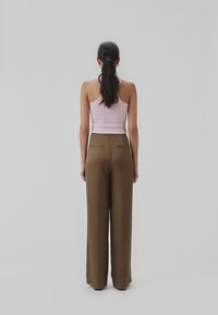 Lyserød, ribbet tanktop parret med løse, brune bukser med vidde, der har baglommer og en glat, flydende tekstur.