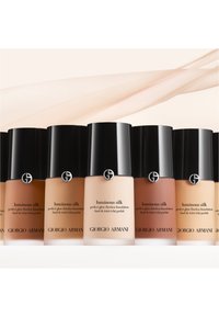 Giorgio Armani Luminous Silk foundation-flasker i varierende hudtoner. Hver flaske har et svart lokk og logo, glatt tekstur og elegant design.