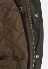 Bruine gequiltte voering met een diagonaal patroon en een donkere buitenstof. Bevat een metalen rits en drukknopen als accenten.