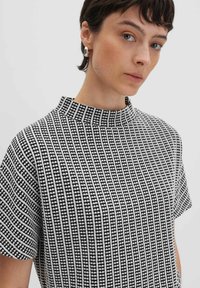 Top a righe in bianco e nero con colletto alto e maniche corte. Presenta un motivo a griglia con piccole forme a cuore e tessuto testurizzato.