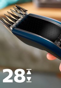 Tagliacapelli cordless con corpo in plastica blu scuro, protezione in metallo per la lama e manopola numerica che mostra le impostazioni di lunghezza, tenuto in mano.