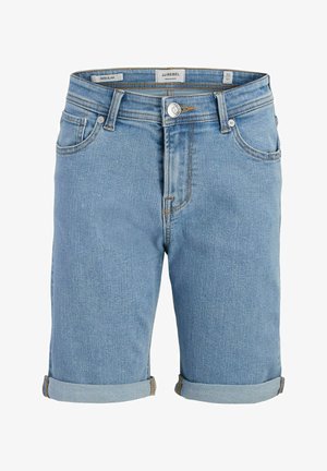 Dreng står med den ene hånd i lommen, iført hvid t-shirt med blåt motiv, opkrogede denimshorts, hvide stribede sokker og sorte sneakers.