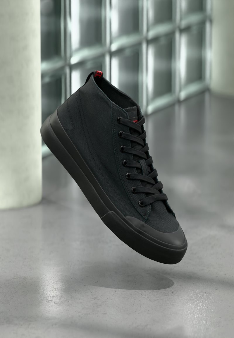 Schwarzer Sneaker in hoher Schnittform mit Obermaterial aus Canvas, rundem Zehenbereich und tonalen Schnürsenkeln. Verfügt über eine Gummisohle und ein kleines rotes Akzent am Absatz.