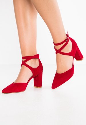 Røde ruskind højhælede sko med spids tå og blokhæl. Har krydsede ankelremme og et åbent hældesign.