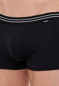 Schwarze Baumwollboxershorts mit einem körperbetonten Design, elastischem Bund mit zwei weißen Streifen und einer glatten Textur. DIM-Logo auf dem Bund.