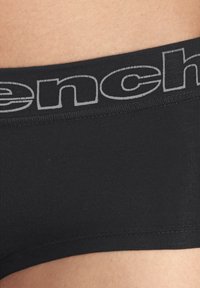 Sous-vêtements en coton stretch noir avec une ceinture élastique grise portant le nom de la marque répété en caractères gras. Texture lisse et design ajusté.