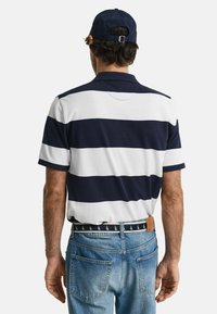 Mörkblå och vit randig polo skjorta för män, kort ärm, med platt krage. Bärs med blå denimjeans och ett mönstrat bälte.