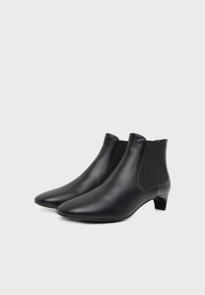 Paire de bottines noires en cuir avec talons bas et panneaux latéraux élastiques sur un fond clair uni.