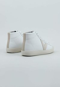 Zapatillas altas blancas con acentos beige, material de cuero suave, costuras en contraste y suela de goma texturizada.