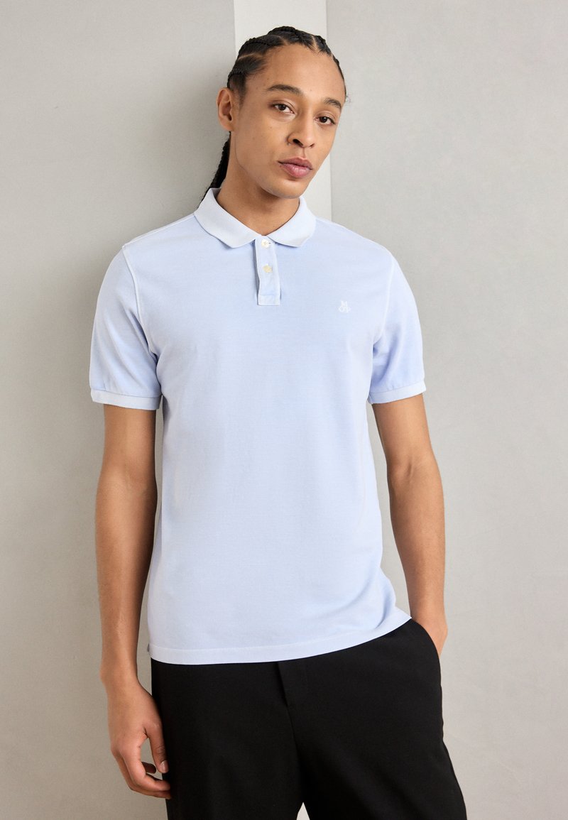 Lyseblå polo skjorte med en solid tekstur, tre-knaps placket og en liten logo på brystet. Stylet med svarte bukser.