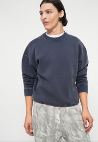 Dark blue sweatshirt made of soft fabric, featuring a round neckline and relaxed fit, with ribbed cuffs. Worn with light gray patterned pants.