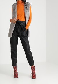 Světle šedá umělá kožešinová vesta přes oranžový rolák, zkombinováno s černými kalhotami s vysokým pasem a červenými kotníkovými botami se vzorem hadí kůže.