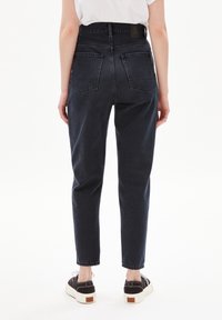 Jean bleu foncé taille haute, coupe slim avec jambes fuselées, présentant deux poches arrière et un détail de ceinture cousue.