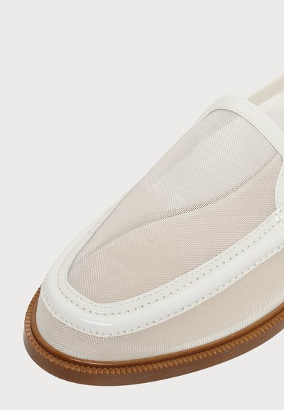 Gros plan d'un mocassin en mesh blanc avec bordure brillante et semelle en caoutchouc marron texturée sur fond clair.