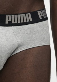 Close-up af en person iført lysegrå underbukser med sort elastik i taljen med stort gråt PUMA-logo.