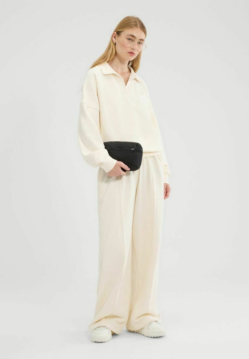 Jasny kremowy oversize'owy sweter z kołnierzykiem i pasującymi spodniami o szerokich nogawkach. Akcesoria to czarna torebka na zamek błyskawiczny i jasne obuwie.