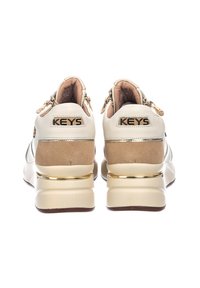 Sneaker crema e beige con colletto imbottito, dettagli in metallo dorato e suola spessa. Presenta il marchio "KEYS" sul tallone.