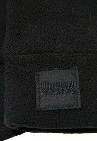 Tissu en polaire noir avec une étiquette cousue portant le texte "URBAN CLASSICS" dans une police texturée, présentant une texture lisse et un aspect doux.
