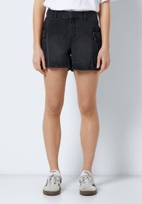 Schwarze Jeans-Shorts haben eine hohe Taille, Seitentaschen und einen lässigen Schnitt. Der Stoff hat eine leicht abgewetzte Struktur.