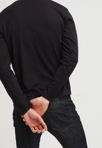 Musta pitkähihaine paita pyöreällä kauluksella, istuva malli, yhdistetty tummansiniset farkut, joissa on takataskut ja näkyvät ompeluyksityiskohdat.