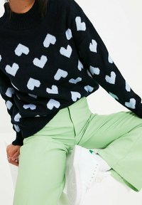 Marineblauer Pullover mit hellblauen Herzmustern, kombiniert mit mintgrünen Hosen und weißen Sneakern. Der Pullover hat einen Rundhalsausschnitt und gerippte Ärmelbündchen.