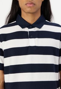 Polo riscas azul-marinho e branco com acabamento texturizado, apresentando colarinho e placket com três botões.